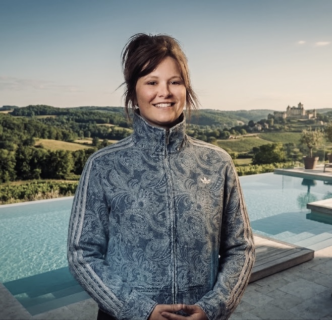 Loulou Motta, founder of CoHost Dordogne, standing by a pool overlooking the Dordogne valley